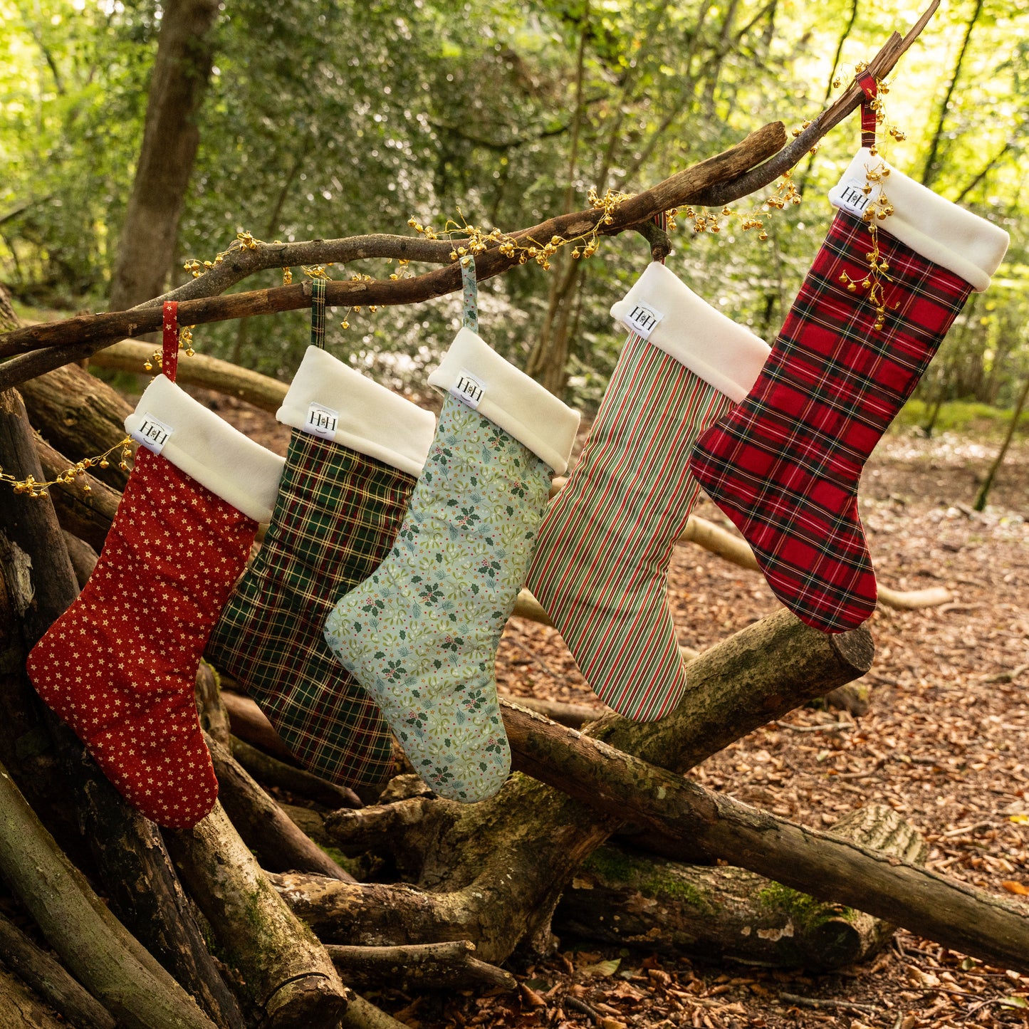 Five Christmas stockings hanging on a branch in a forest setting